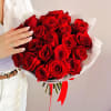 Handheld bouquet of deep red roses wrapped in white paper with a red ribbon.