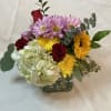 Mixed bouquet of roses, daisies, hydrangea, and sunflowers in a glass vase