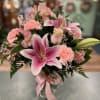 Pink lilies and carnations arranged in a glass vase with a pink ribbon.