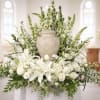 White floral arrangement with lilies and roses around a urn in a church setting