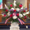 Tall red, white, and purple flower arrangement in a white urn with patriotic ribbon on a pedestal