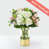 Bouquet of white and pink flowers in a clear glass vase with a gold base