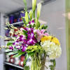 Tall mixed arrangement with white calla lilies, purple orchids, pink lilies, and yellow blooms in a round glass vase