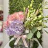 Pastel arrangement of pink roses, lavender hydrangea, and lilies in a glass cube vase with a pink ribbon.