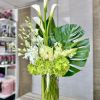 Tall white and green arrangement with calla lilies, orchids, and hydrangeas in a clear glass cylinder vase
