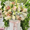 Round hatbox arrangement of pale pink and white roses with pink berries and foliage, tied with a pink ribbon.