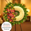 Crescent standing wreath with white blooms, pink lilies, red and yellow flowers on a green leaf base.