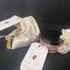 Two satin gift pouches and a pink jar with a black lid on a dark surface