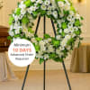 Large white and green floral wreath on a black metal easel in a chapel.