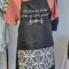 Black apron with white text over a pink shirt