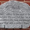Engraved memorial stone with a quote against a brick wall.