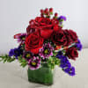 Red roses and purple daisies arranged in a square glass vase