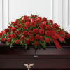 Red rose and carnation casket spray with ribbon on a dark casket