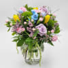 A clear glass vase full of spring flowers and tiny eggs and