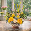 A cheerful spring arrangement featuring vibrant yellow roses, soft carnations, delicate waxflower