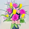 Arrangement of bright pink roses, yellow tulips, and pastel blooms in a black vase with a pink butterfly decoration