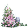 Pink lilies and roses arranged beside a silver cremation urn.
