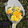 A bright wrapped handheld bouquet of yellow roses and seasonal blooms, accented