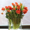 Colorful tulips and seasonal flowers in clear square vase. Shown in orange