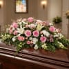 A graceful casket spray featuring soft pink roses, lilies, and delicate seasonal