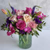 Mixed bouquet of pink roses, carnations, and tulips with purple accents in a textured green glass vase