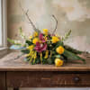 Low arrangement of yellow roses, pink orchids, and white snapdragons on a rustic wooden table