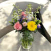 Mixed bouquet of pink roses, yellow gerbera daisy, and pastel flowers in a clear glass vase