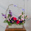 Pink and purple floral arrangement in a wooden box with butterfly picks