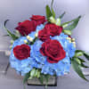 This arrangement has red roses, blue hydrangeas, white alstroemeria and white Hypericum