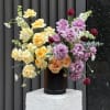 Soft yellow and peach roses mingle with lavender roses and burgundy button