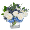 Low arrangement of white roses and blue hydrangeas in a clear glass cube vase