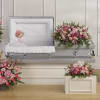 Soft pink roses and lilies drape gently across a casket in this