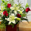 Delicate red roses with soft white lillies in and square vase.