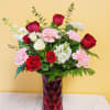 Red roses, pink carnations, and white blooms in a faceted red glass vase