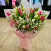 Hand-tied bouquet of pink and white tulips with small white filler flowers wrapped in pink paper and ribbon.