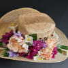A whimsical straw hat adorned with faux florals and delicate greenery. Designed