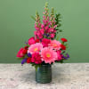 Tall pink floral arrangement with gerbera daisies, roses, and snapdragons in a green glass vase