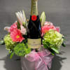 Champagne bottle in a pink floral gift arrangement with a ribbon