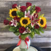 Bouquet of red roses, sunflowers, and lilies in a glass vase with a red ribbon
