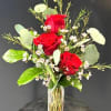 Three vivid red roses stand upright in a slim clear glass cylinder