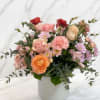 This lush arrangement features delicate blush pinks, creamy peaches, and rich pops