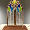 A small arched stained-glass panel standing on a tiered wood base creates