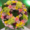 Sympathy wreath featuring yellow, pink, purple and green spring blooms.