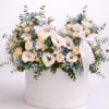 Low arrangement of white and peach flowers with blue accents in a round white hat box with ribbon