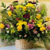 Large woven basket overflowing with yellow roses, pink spray roses, purple blooms