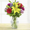 Bouquet of red roses, yellow lilies, and purple flowers in a clear glass vase