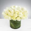 White roses in a low glass cylinder vase with decorative green wrap