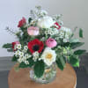 Mixed arrangement of red, pink, and white flowers in a clear glass vase on a wooden table