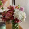 Mixed bouquet of pink alstroemeria, white hydrangeas, and a pink rose in a clear glass vase on a table