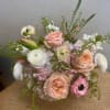 A soft, pastel arrangement built around peach roses and white ranunculus creates